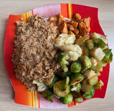 Ein Teller mit Reis, gebratenem Gemüse und mariniertem Hähnchen.