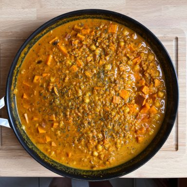 Bunte Linsensuppe mit Gemüse in einer schwarzen Pfanne auf einem Holzbrett.