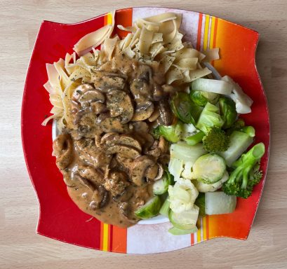 Pasta mit Pilzsauce, dazu ein gemischter Salat auf einem roten Teller.