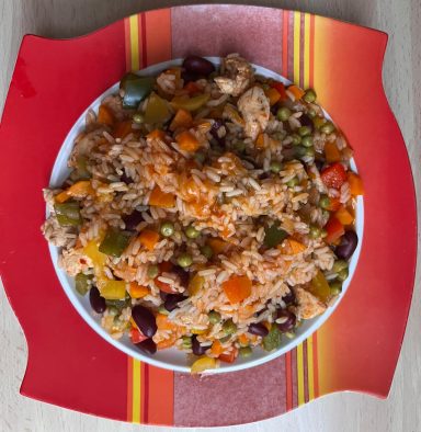 Bunte Reispfanne mit Gemüse und Fleisch auf einem roten Teller serviert.